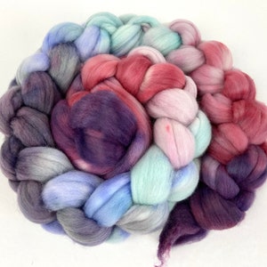May include: A braided bundle of colourful wool yarn in shades of purple, pink, blue, and grey. The yarn is arranged in a spiral shape, with the different colours blending together.