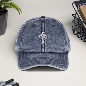 May include: A blue denim baseball cap with a white embroidered cross design.
