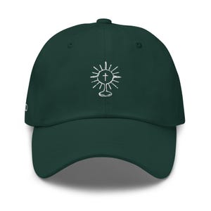 May include: A dark green baseball cap featuring a white embroidered design of a sun with a cross inside. The design is centrally positioned on the front of the cap.