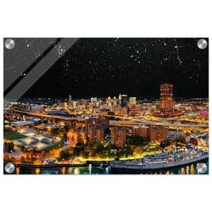 Puede incluir: Impresión de un paisaje urbano nocturno con edificios iluminados, carreteras y una zona marítima. La obra presenta un cielo oscuro y estrellado y está montada con herrajes plateados. Captura la esencia de la vida urbana.