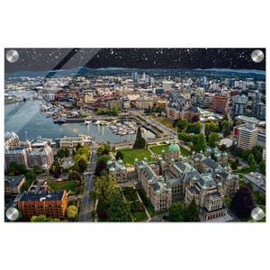 May include: An aerial view of a city harbor at night featuring a large stone building with a green dome in the foreground, a marina filled with boats, and a dense urban skyline under a dark, starry sky with four silver mounting bolts.