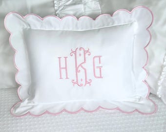 May include: White rectangular pillow with a pink scalloped edge and pink embroidered monogram. The pillow is on a white bedspread. The monogram features the letters H, K, and G in a decorative font.