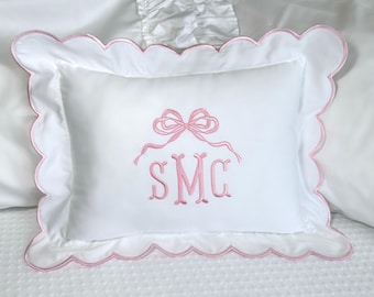 Puede incluir: Almohada rectangular blanca con borde festoneado rosa y lazo y monograma bordados en rosa. El monograma presenta las letras "SMC" en una escritura delicada, añadiendo un toque personalizado a la ropa de cama.