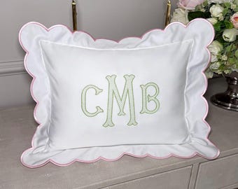 May include: White rectangular pillow with a scalloped edge, trimmed in pink. The pillow features the embroidered initials "CMB" in a light green color. The pillow is placed on a light gray surface.