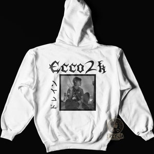 May include: White hooded sweatshirt with black text that reads "Ecco2k" and a black and white photo of a person sitting down. The text "ドレイク" is written vertically in Japanese on the left side of the photo.