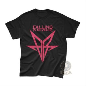 May include: Black t-shirt featuring a pink graphic design with the text "FALLING IN REVERSE" above a star-shaped emblem. The shirt is made of a soft material and is suitable for casual wear. The design is centered on the front of the shirt.