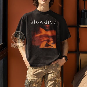 以下が含まれることがあります： 顔と「slowdive」と「just for a day」の文字がプリントされた黒いTシャツ。画像の人物は、Tシャツ、サングラス、迷彩柄のパンツを着用している。