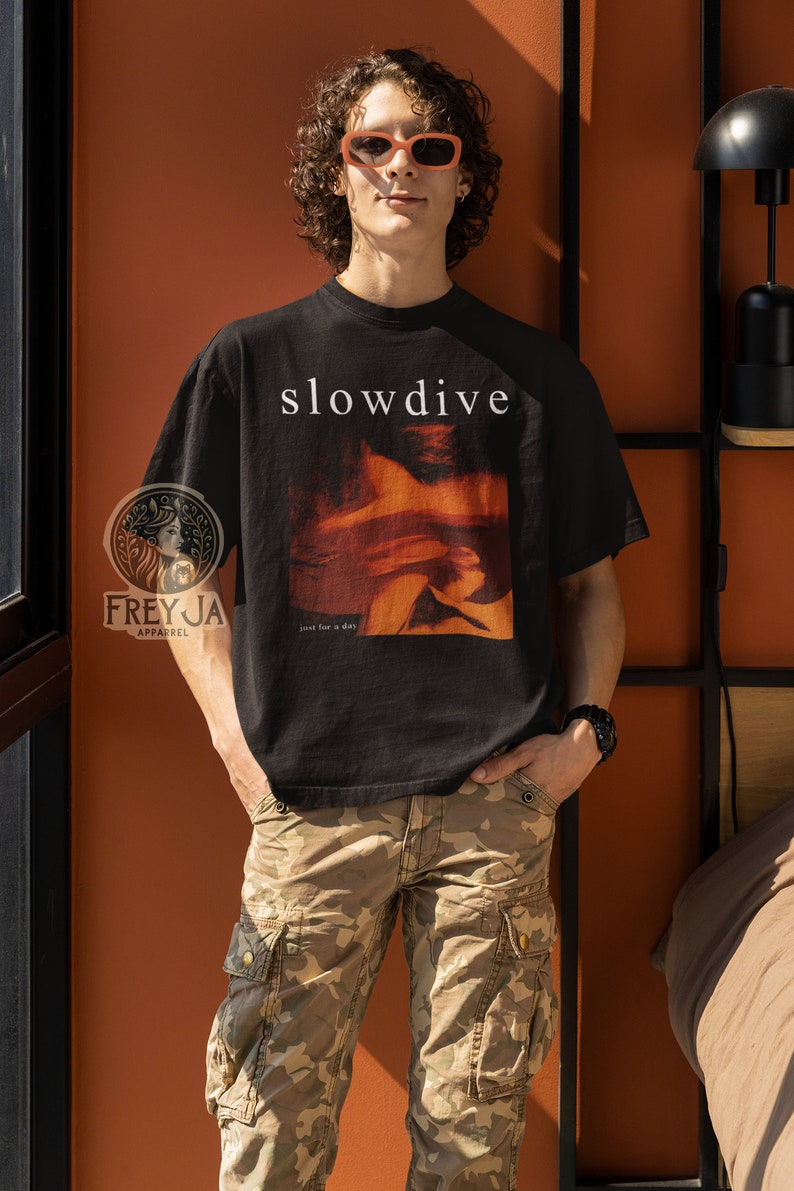 以下が含まれることがあります： 顔と「slowdive」と「just for a day」の文字がプリントされた黒いTシャツ。画像の人物は、Tシャツ、サングラス、迷彩柄のパンツを着用している。