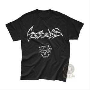 Pode incluir: Camiseta preta com um gráfico branco de uma caveira usando uma bandana e a palavra "Sacredless" em uma fonte estilizada. A camiseta é de gola redonda.