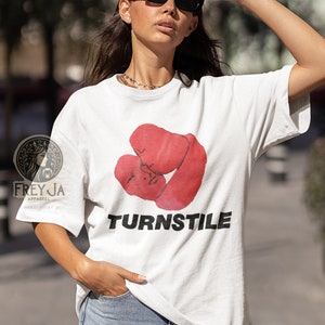 May include: White t-shirt with a red graphic of two boxing gloves and the word "TURNSTILE" printed in black.