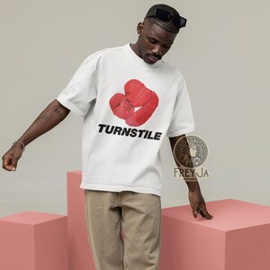 May include: White t-shirt with a red graphic of two figures embracing in the shape of a heart. The text "TURNSTILE" is printed in black below the graphic.
