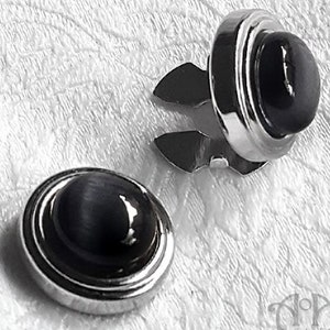 May include: Two silver-toned shirt studs with black cat's eye stones. The studs have a decorative ring around the stone.