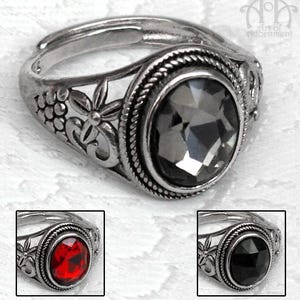 May include: Silver ring with an oval, faceted, grey gemstone. The ring has detailed floral and rope patterns around the bezel and band. Additional images show the ring with red and black gemstones.
