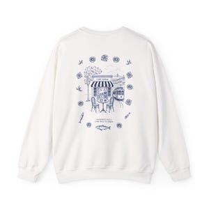 May include: White sweatshirt with a blue illustration on the back depicting a cafe, tram, and fish. The text reads "I WONDER IF YOU'LL COME BACK TO LISBON."