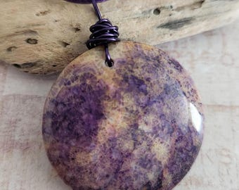 May include: A round pendant necklace with a purple and tan marbled design. The pendant is suspended from a purple cord. The wire wrap at the top of the pendant is also purple. The necklace is a unique piece of jewelry.