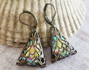 May include: A pair of antique brass-toned earrings. Each earring features a filigree cone shape with iridescent, colorful glass inserts. The earrings have lever-back closures and are displayed on a seashell.