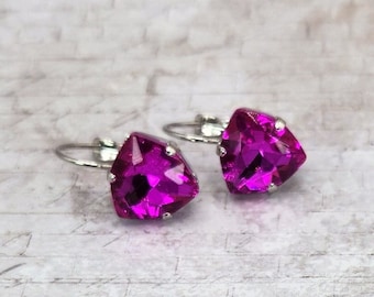 May include: A pair of magenta-colored, triangular-shaped earrings with silver-colored metal findings. The earrings are set against a white and gray brick-patterned background.