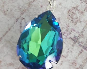 May include: A silver necklace featuring a large, teardrop-shaped pendant. The pendant is a vibrant mix of blue and green, with a faceted design that catches the light. The chain is delicate and silver.