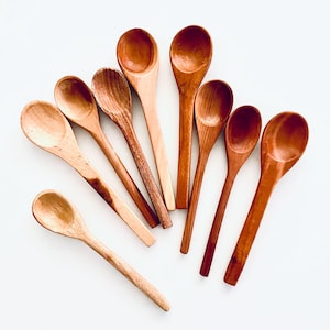 May include: A set of eight wooden spoons in various sizes, all with a natural wood finish. The spoons are arranged in a fan shape on a white background.
