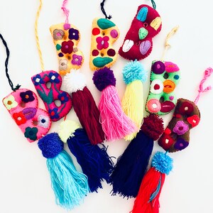May include: A set of seven colorful felt letter charms with embroidered flowers and pom-pom tassels. The letters are all the letter "B" and are in various colors, including pink, green, yellow, and red.