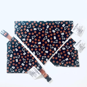May include: A black pet bandana featuring a repeating pattern of orange basketballs and white basketball jerseys with the number 2. The bandana includes an orange adjustable collar with a black plastic buckle and a Chick Rocks brand tag.