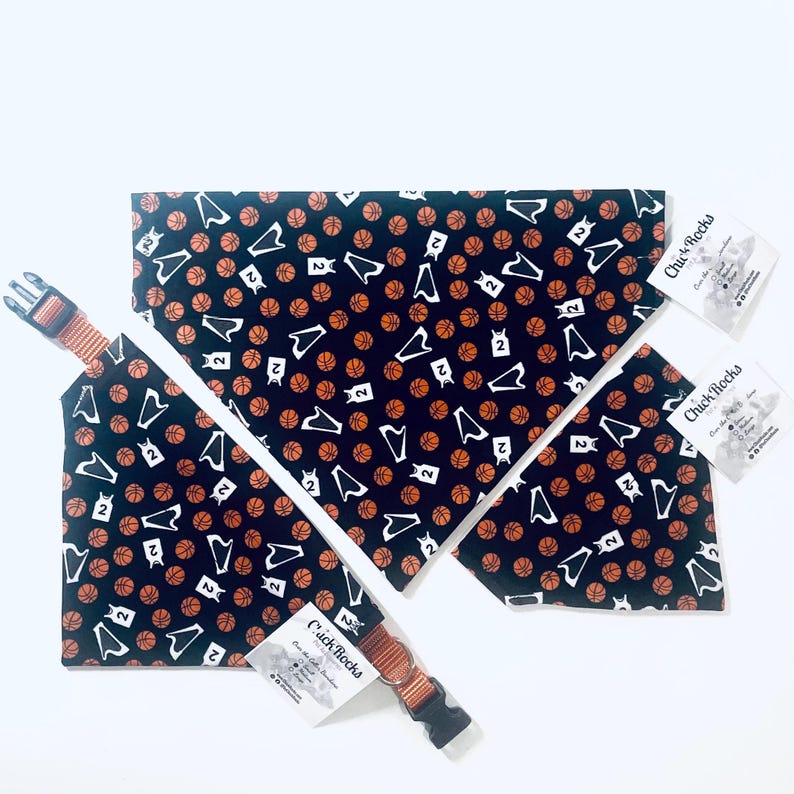 May include: A black pet bandana featuring a repeating pattern of orange basketballs and white basketball jerseys with the number 2. The bandana includes an orange adjustable collar with a black plastic buckle and a Chick Rocks brand tag.
