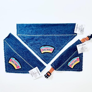 May include: Blue denim dog bandanas and collar with the San Antonio Spurs logo patch. The bandanas are triangular and the collar has an orange and black buckle. Each item has a Chick Rocks tag.