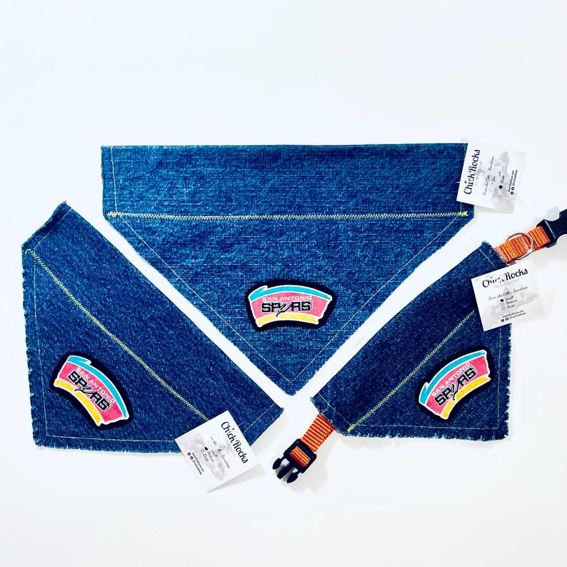 May include: Blue denim dog bandanas and collar with the San Antonio Spurs logo patch. The bandanas are triangular and the collar has an orange and black buckle. Each item has a Chick Rocks tag.