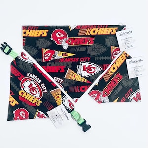 May include: A black pet bandana and collar set with a repeating pattern of the Kansas City Chiefs logo, helmets, and text in red, yellow, and white. The collar is green with a black buckle.