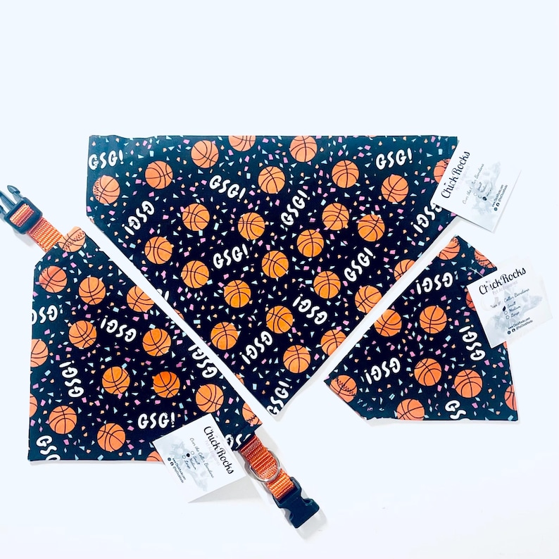 Puede incluir: Un conjunto de collar y pa&ntilde;uelo para perros con tem&aacute;tica de baloncesto. La tela negra est&aacute; estampada con balones de baloncesto naranjas, confeti y el texto "GSG!". El collar tiene una hebilla naranja y negra.