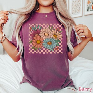 May include: A purple t-shirt with a graphic of a bouquet of flowers in a pink and white checkered pattern.