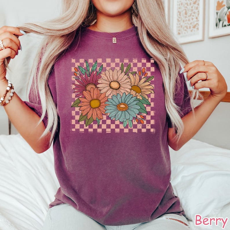 May include: A purple t-shirt with a graphic of a bouquet of flowers in a pink and white checkered pattern.