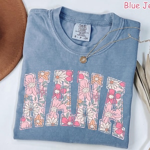 May include: A blue jean t-shirt with a floral design spelling out "MAMA". The shirt has a distressed look and is made of a soft, comfortable fabric.