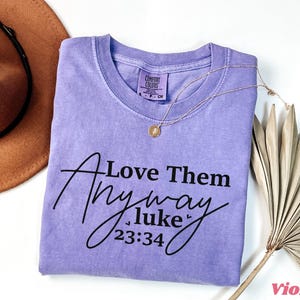 May include: A purple t-shirt with the text "Love Them Anyway Luke 23:34" printed in black.