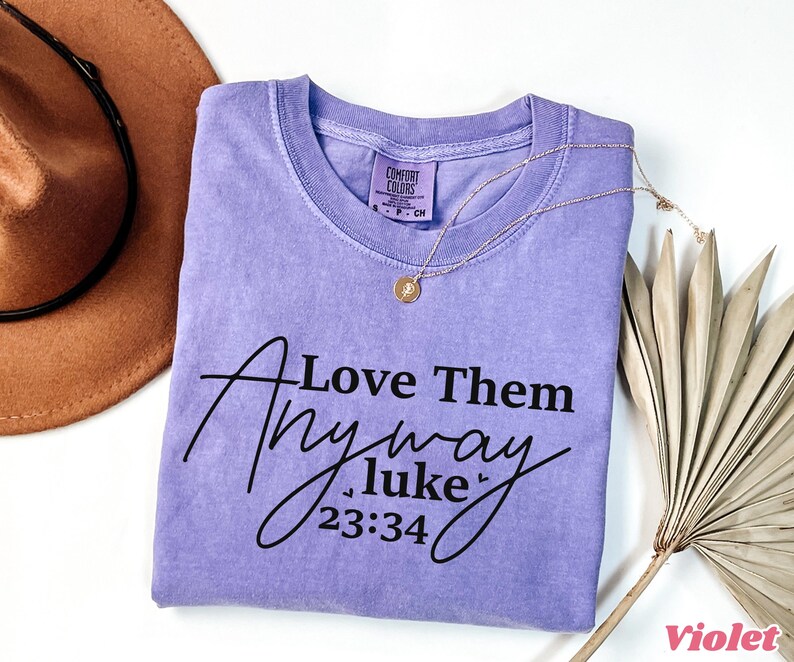 May include: A purple t-shirt with the text "Love Them Anyway Luke 23:34" printed in black.