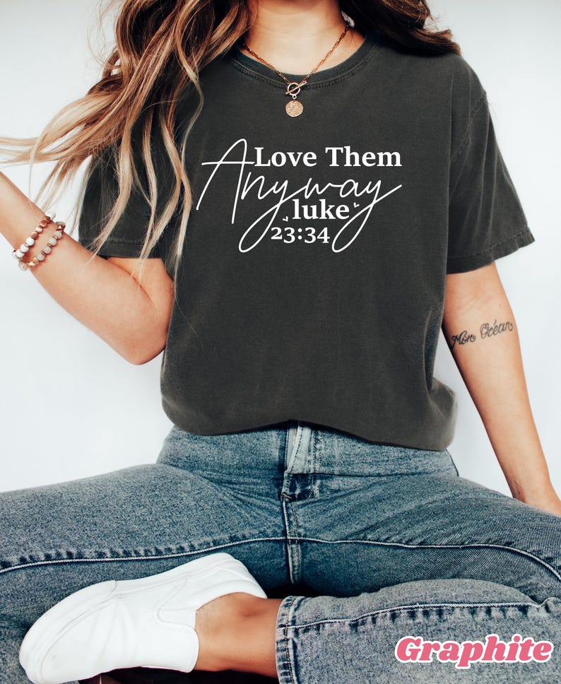 May include: A dark gray t-shirt with the text "Love Them Anyway Luke 23:34" in white.