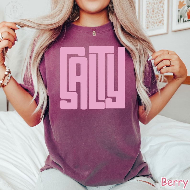 May include: Berry-colored t-shirt with the word "GALY" in a large, pink, block letter design. The shirt has short sleeves and a crew neck. The word "Berry" is printed in the bottom right corner.