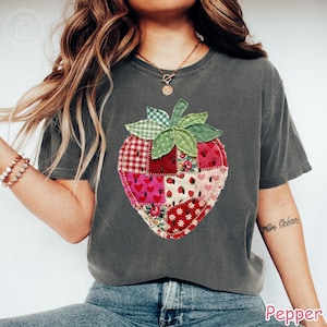May include: Dark gray t-shirt featuring a patchwork strawberry design. The strawberry is composed of various fabric patterns, including hearts, floral prints, and gingham. The word "Pepper" is printed at the bottom right.