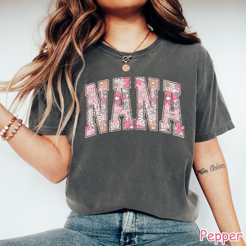 May include: A gray t-shirt with a floral print design that reads "NANA" in a vintage collegiate style.