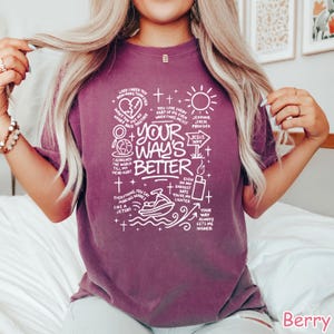 Op de afbeelding: Bessenkleurig T-shirt met de witte tekst "Your Way's Better", vergezeld van diverse afbeeldingen en zinnen. Het ontwerp bevat een hart, een zon, een jetski en andere symbolen. Het T-shirt heeft een ronde hals.