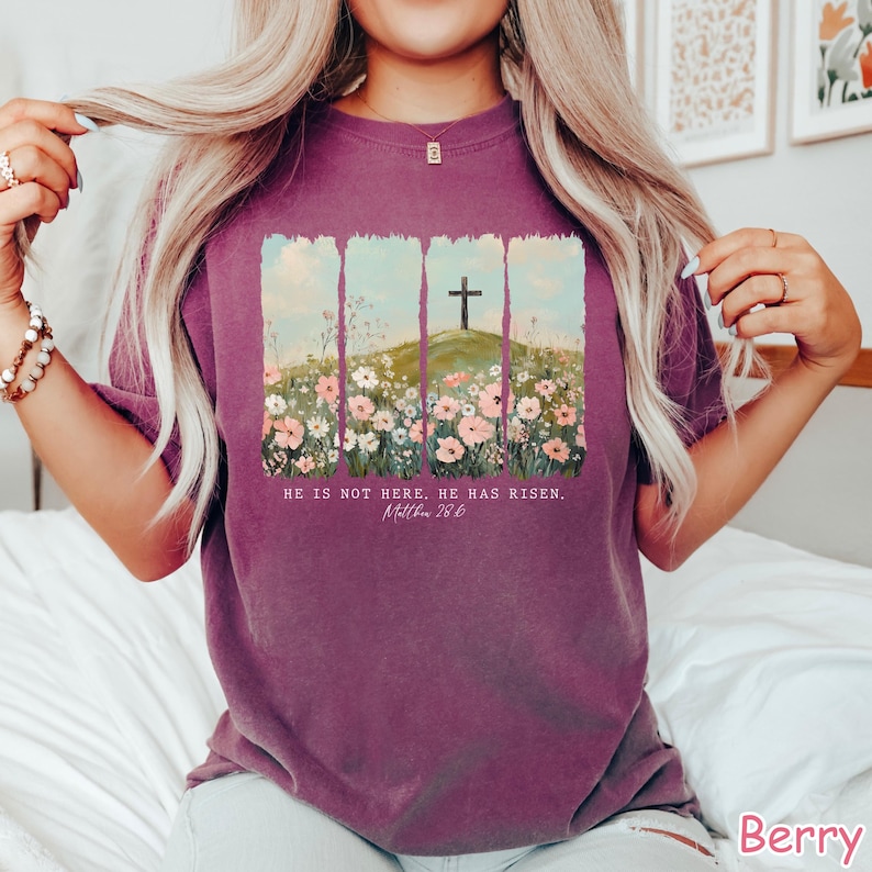 May include: Purple t-shirt with a floral design and a cross on a hill. The text "He is not here, He has risen. Matthew 28:6" is printed on the shirt.