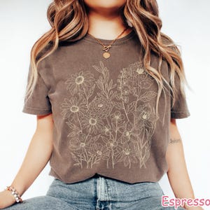 Puede incluir: Camiseta color espresso con un dise&ntilde;o floral beige. El gr&aacute;fico incluye varias flores y follaje. La camiseta tiene mangas cortas y cuello redondo. La palabra "Espresso" est&aacute; impresa en la parte inferior derecha.