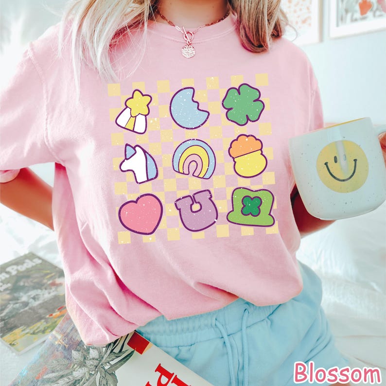 Peut inclure: Un t-shirt rose avec un motif &agrave; carreaux et diverses images de dessins anim&eacute;s color&eacute;s, notamment un arc-en-ciel, un fer &agrave; cheval, un tr&egrave;fle, une licorne, un c&oelig;ur et une &eacute;toile. Le t-shirt a un col rond et des manches courtes.