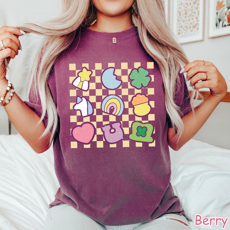 Peut inclure: Un t-shirt violet &agrave; motif &agrave; carreaux avec une vari&eacute;t&eacute; d'images de dessins anim&eacute;s color&eacute;s, notamment un arc-en-ciel, un fer &agrave; cheval, un tr&egrave;fle &agrave; quatre feuilles, un pot d'or, une licorne et une &eacute;toile.