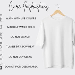 May include: A white t-shirt hangs on a wooden hanger. The shirt is plain and has short sleeves. To the left are care instructions with icons and text: Wash with like colors, machine wash cold, do not bleach, tumble dry low heat, do not dry clean, and do not iron design area.