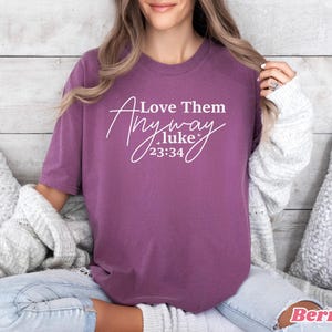 May include: Purple t-shirt with white text that reads "Love Them Anyway .luke 23:34".