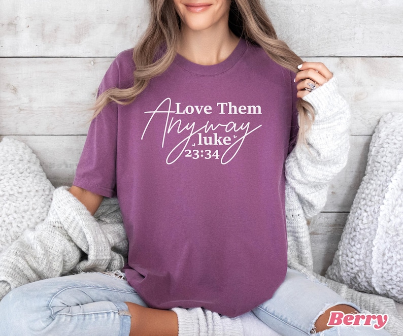 May include: Purple t-shirt with white text that reads "Love Them Anyway .luke 23:34".