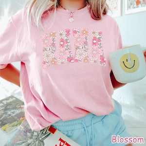 May include: A pink t-shirt with a floral design spelling out "MAMA".