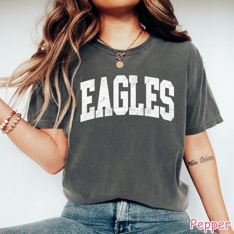 May include: A dark grey t-shirt featuring the word "EAGLES" in large, white, block letters. The shirt has a crew neck and short sleeves. The fabric appears soft and comfortable.