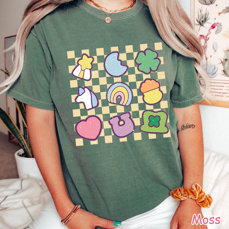Peut inclure: T-shirt vert avec un motif &agrave; carreaux et diverses images de dessins anim&eacute;s color&eacute;s, notamment un arc-en-ciel, un fer &agrave; cheval, un tr&egrave;fle, un c&oelig;ur, une licorne, une &eacute;toile, un croissant de lune et un chapeau de lutin.